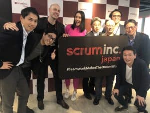 Members of Scrum Inc. and KDDI holding a sign that reads Scrum Inc Japan hashtag Team Work Makes the Dream Work