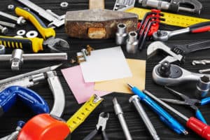 Set of tools, pen, and sticky note over a wood background.