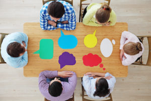 Team of business people in casual clothes sitting around the table with paper dialog boxes, discussing opinion concept