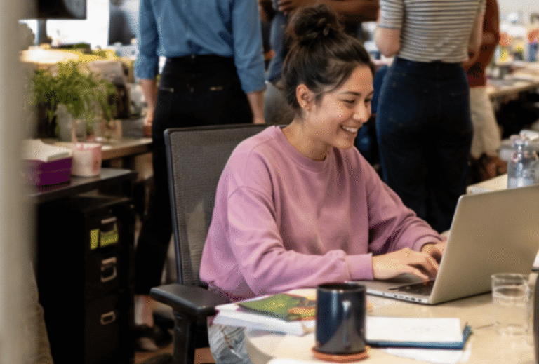 Woman participating in Generative AI training, working on a laptop in a collaborative office setting.