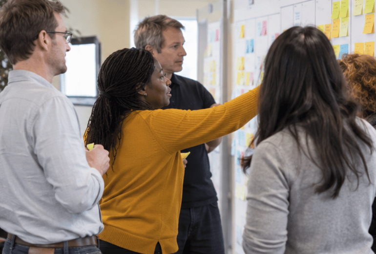 Professionals coordinating work at a visual planning board during a collaborative Scrum@Scale workshop.